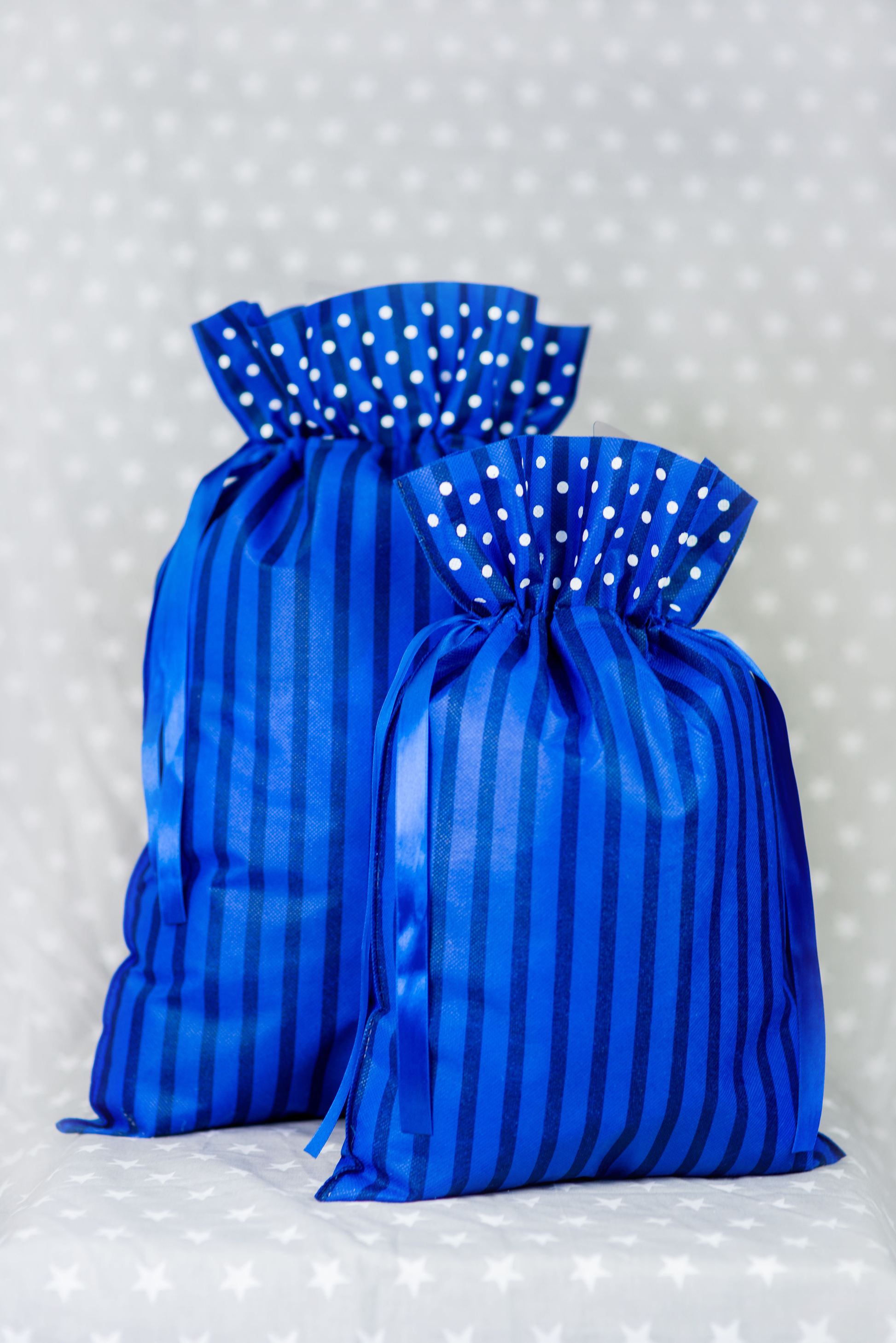 Dwa granatowe worki prezentowe w paski i białe kropki, ustawione obok siebie na tle w gwiazdki.