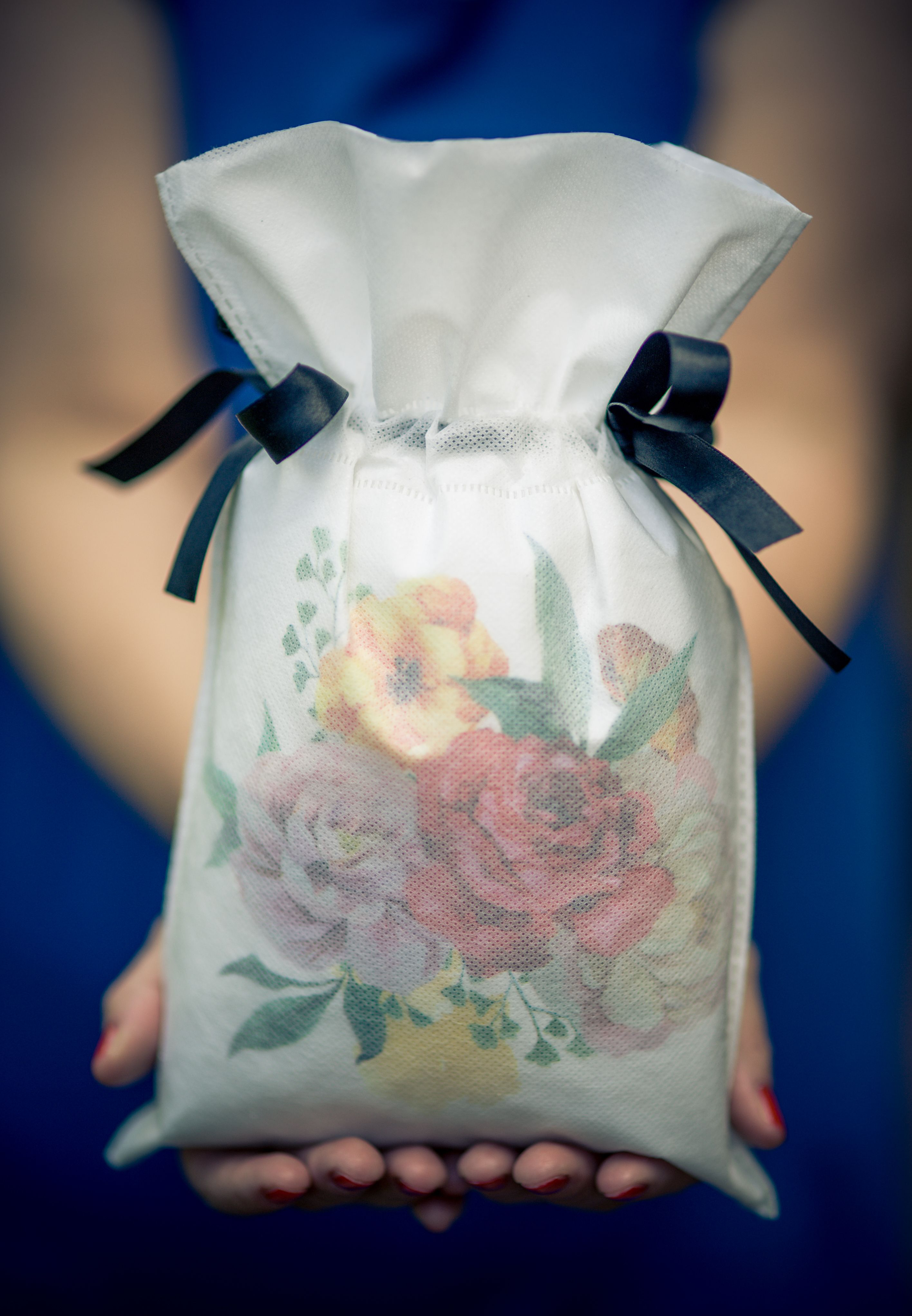 Biały worek prezentowy z motywem kolorowych róż i czarnymi satynowymi wstążkami, trzymany w dłoniach.