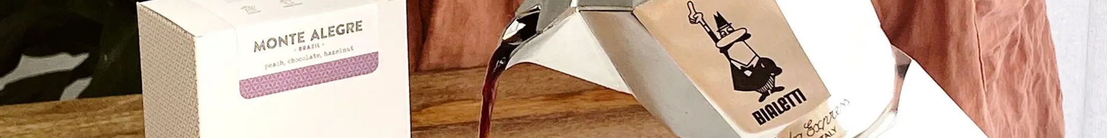 Kawiarka Bialetti podczas parzenia kawy obok pudełka ziaren Monte Alegre na drewnianym stole.