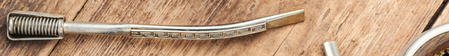 Metalowa bombilla do picia yerba mate, ozdobiona wzorem geometrycznym, leżąca na drewnianym tle.