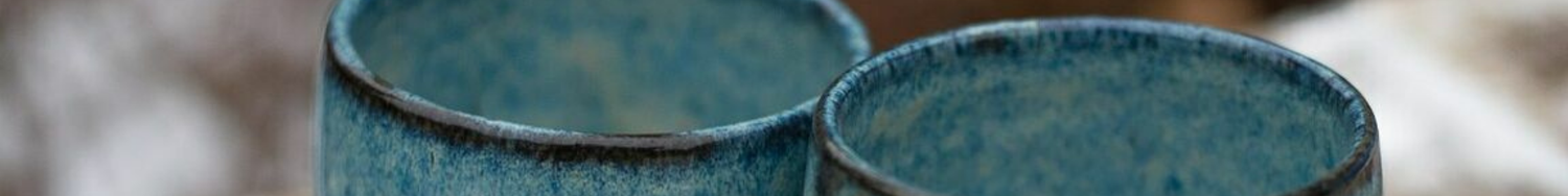 Dwie niebieskie czarki ceramiczne o delikatnej fakturze, ustawione obok siebie na rozmytym tle.