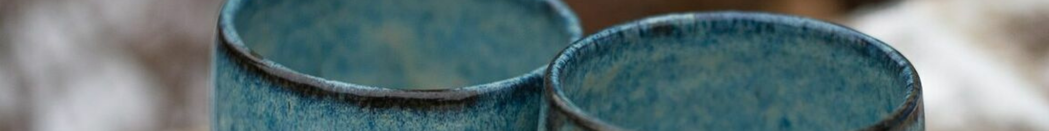 Dwie niebieskie czarki ceramiczne o delikatnej fakturze, ustawione obok siebie na rozmytym tle.