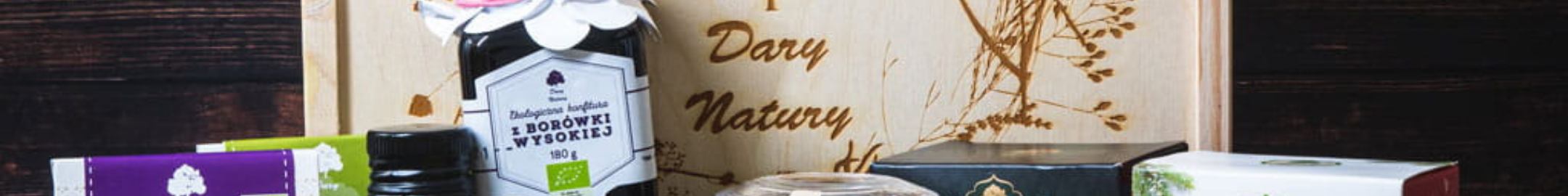 Zestaw produktów marki Dary Natury w drewnianej skrzynce, zawierający m.in. herbaty i ekologiczny konfitur z borówki.