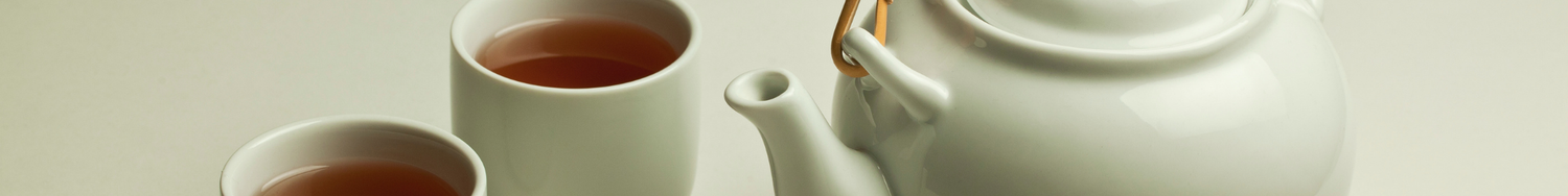 Biały porcelanowy dzbanek do herbaty z dwoma filiżankami wypełnionymi naparem.