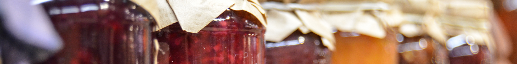 Słoiki z domowymi dżemami i konfiturami owocowymi przykryte papierowymi nakrywkami.