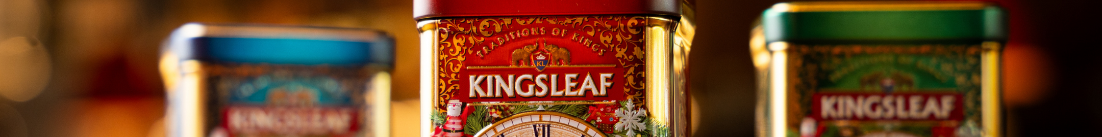 Metalowe puszki herbaty Kingsleaf w ozdobnych opakowaniach, z widocznym logo na czerwonym tle.