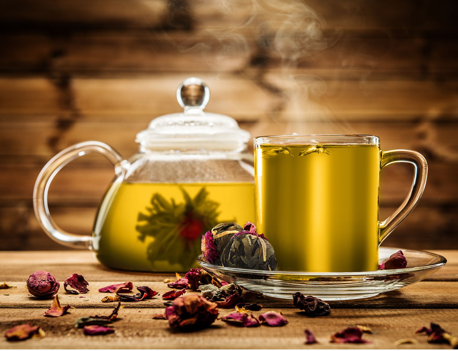 Szklany dzbanek i filiżanka z zaparzoną herbatą rozkwitającą Rich Flower w otoczeniu płatków róż.