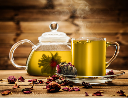 Szklany dzbanek i filiżanka z zaparzoną herbatą rozkwitającą Rich Flower w otoczeniu płatków róż.