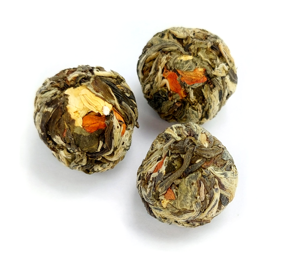 Herbata rozkwitająca Lily Fairy w formie trzech zwiniętych kulek z widocznymi kwiatami przeznaczona do zaparzania w szklanym naczyniu.
