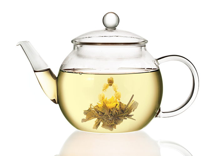 Szklany dzbanek z jasnym naparem białej herbaty oraz rozwiniętym kwiatem herbaty rozkwitającej Autumn Beauty.
