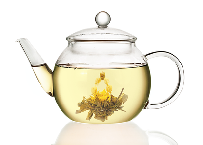 Szklany dzbanek z jasnym naparem białej herbaty oraz rozwiniętym kwiatem herbaty rozkwitającej Autumn Beauty.
