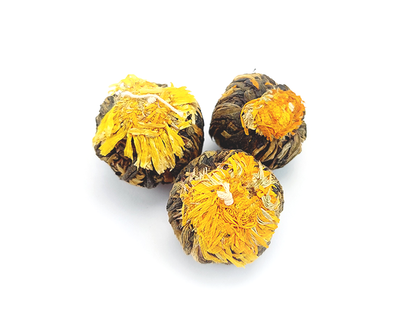 Trzy kulki herbaty rozkwitającej Czarna Perła z widocznym żółtym kwiatem w centrum.