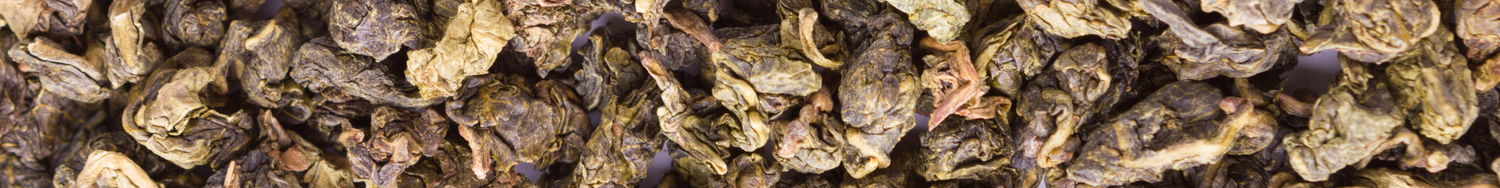 Zbliżenie na suszone liście herbaty Oolong – zwinięte, ciemnooliwkowe listki tworzące naturalne tło.