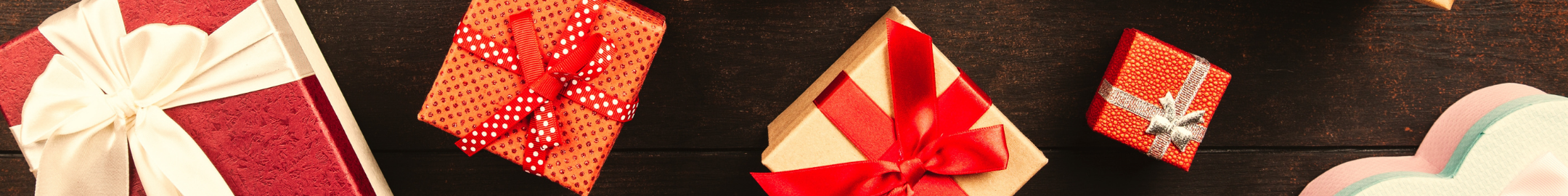 Kolorowe pudełka prezentowe owinięte wstążkami w różnych wzorach i kolorach, ułożone na drewnianym tle.