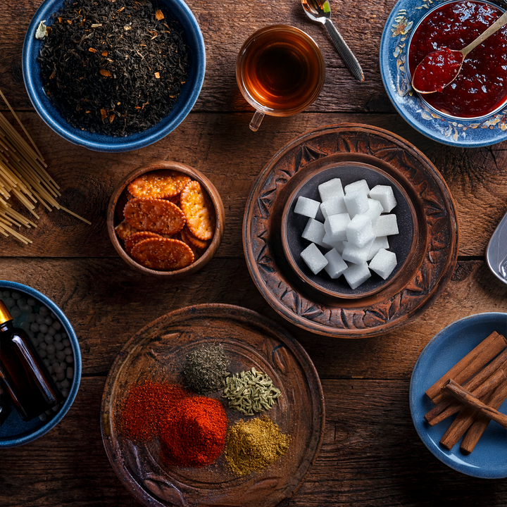 Na drewnianym stole w miseczkach znajduje się dżem, przyprawy, cukier w kostkach oraz filiżanka z czarną herbatą 