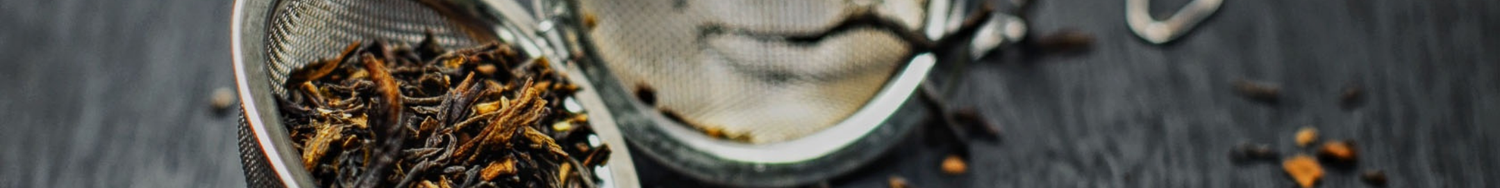 Metalowe zaparzacze do herbaty z suszem liściastym na ciemnym tle.